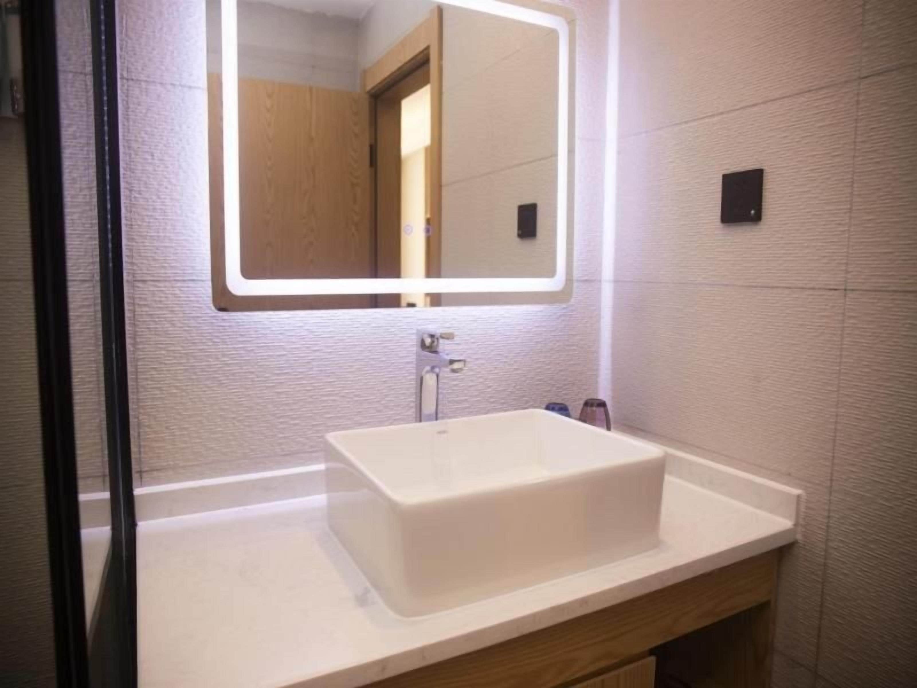 Un baño con un lavamanos rectangular, un espejo con marco iluminado y un mueble de madera debajo.