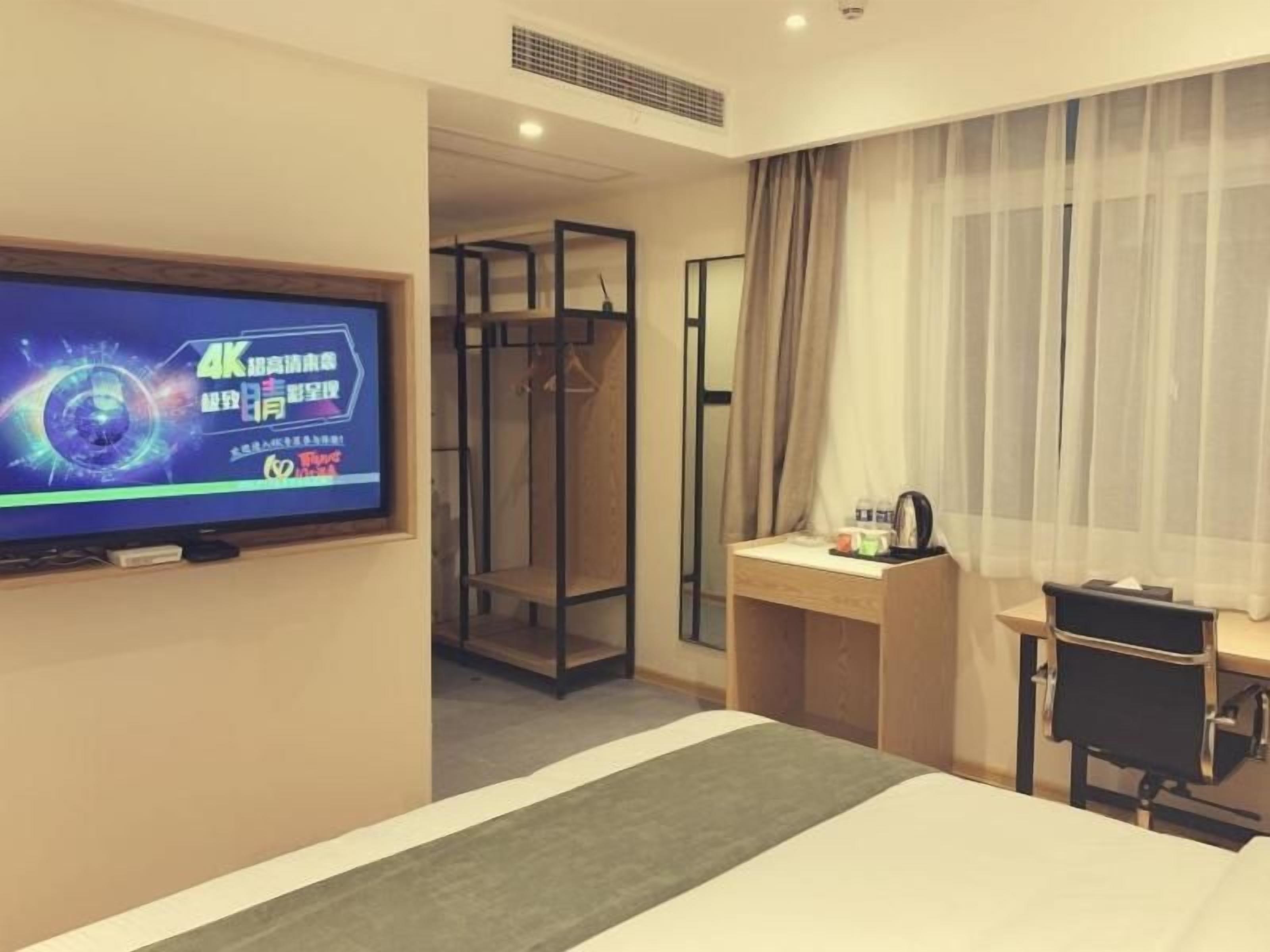 Habitación de hotel con cama, escritorio con silla, televisión, espejo y vestidor.