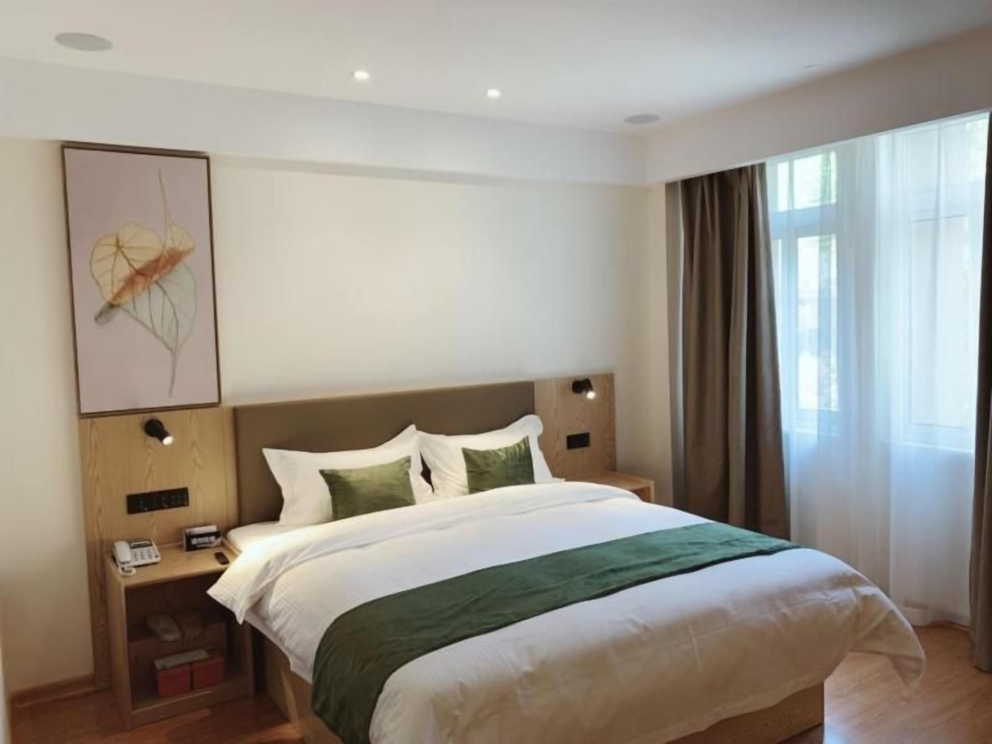 A hotel room with a bed, bedside tables, a wall-mounted artwork, and a window with curtains.