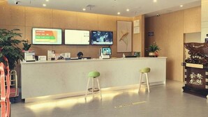 A reception area with a wooden reception desk, two green stools, and two monitors displaying information. - Greentree Inn Express Jiangsu Suqian Shuyang County Bus Station (Suqian)