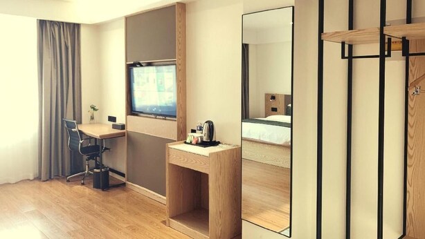 A modern hotel room with a wooden desk, a chair, a small table with a kettle, a large mirror, and a bed with a wooden headboard. - Greentree Inn Express Jiangsu Suqian Shuyang County Bus Station (Suqian)