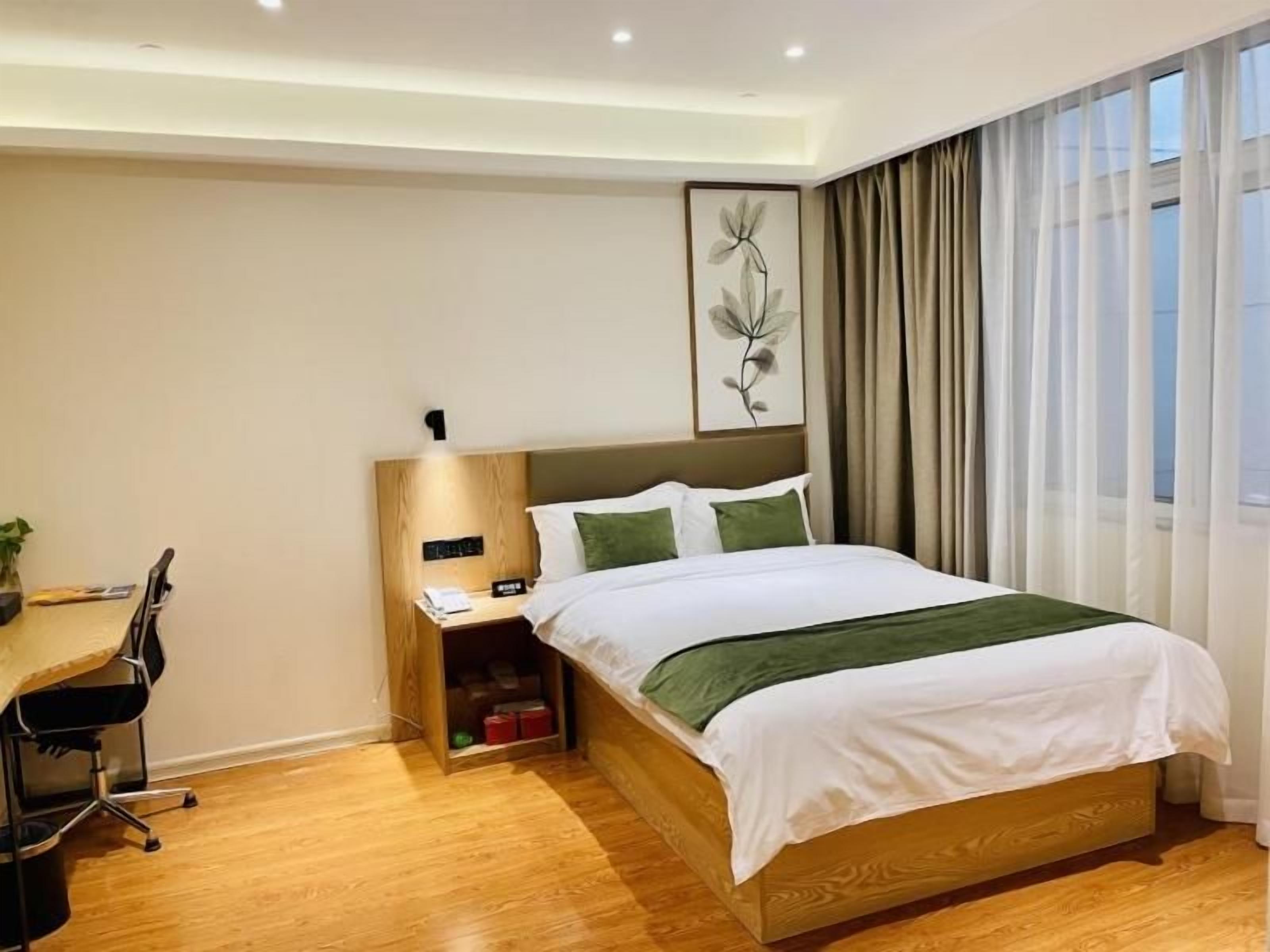 Habitación de hotel con cama de madera, un escritorio con silla, mesita de noche y un ventanal con cortinas.