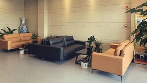 A modern lobby with a black leather sofa, a beige sofa, and a coffee table. There are potted plants and a vase on the floor. - Greentree Inn Express Jiangsu Suqian Shuyang County Bus Station (Suqian)