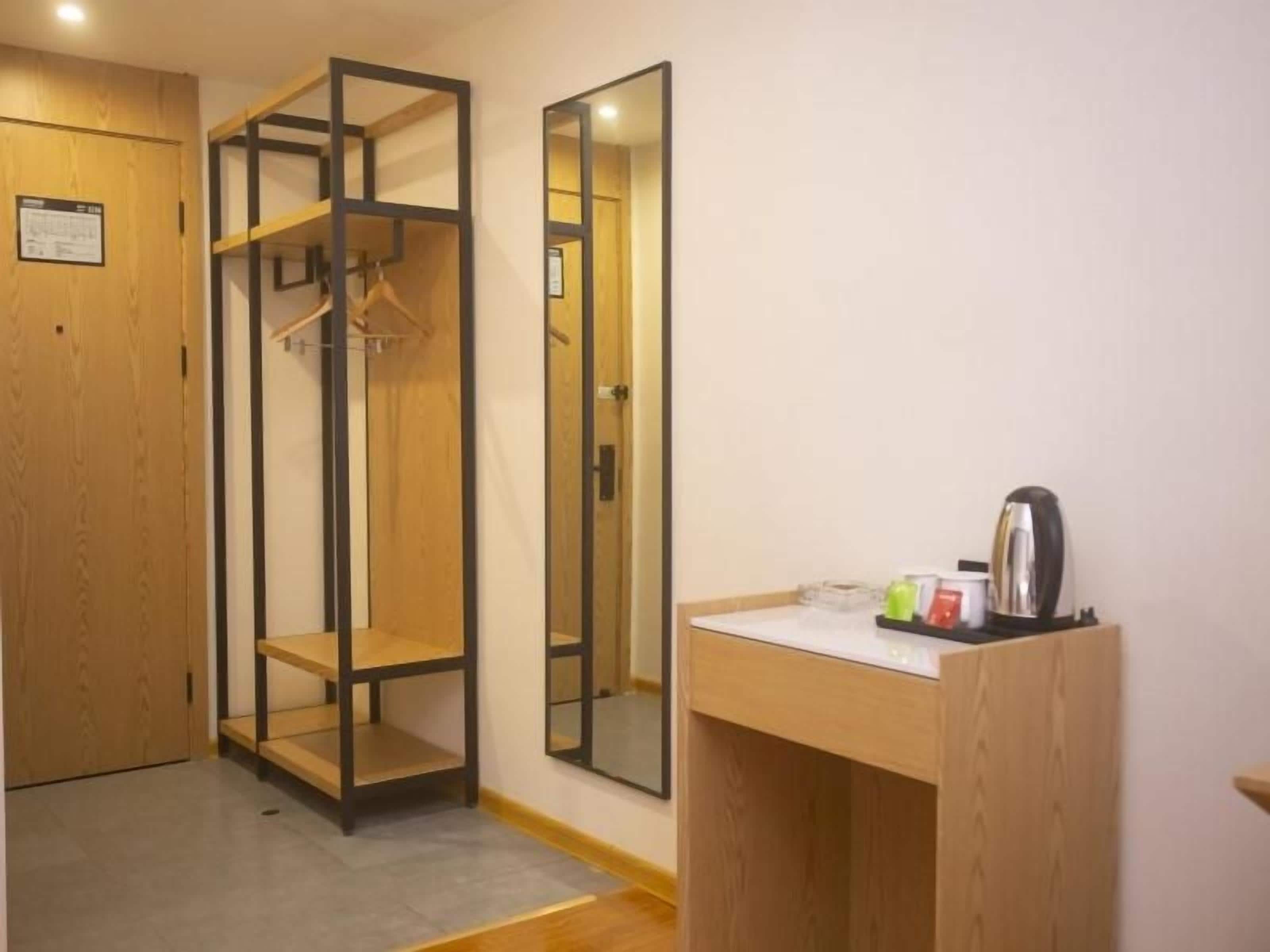 Quarto com guarda-roupa de madeira, espelho e uma pequena mesa com chaleira e chávenas.