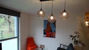 Un salon moderne avec une grande fenêtre, une table basse en verre, un canapé bleu, un pouf orange et trois lampes suspendues.