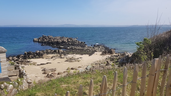 Une plage rocheuse offrant une vue dégagée sur la mer et les montagnes lointaines.