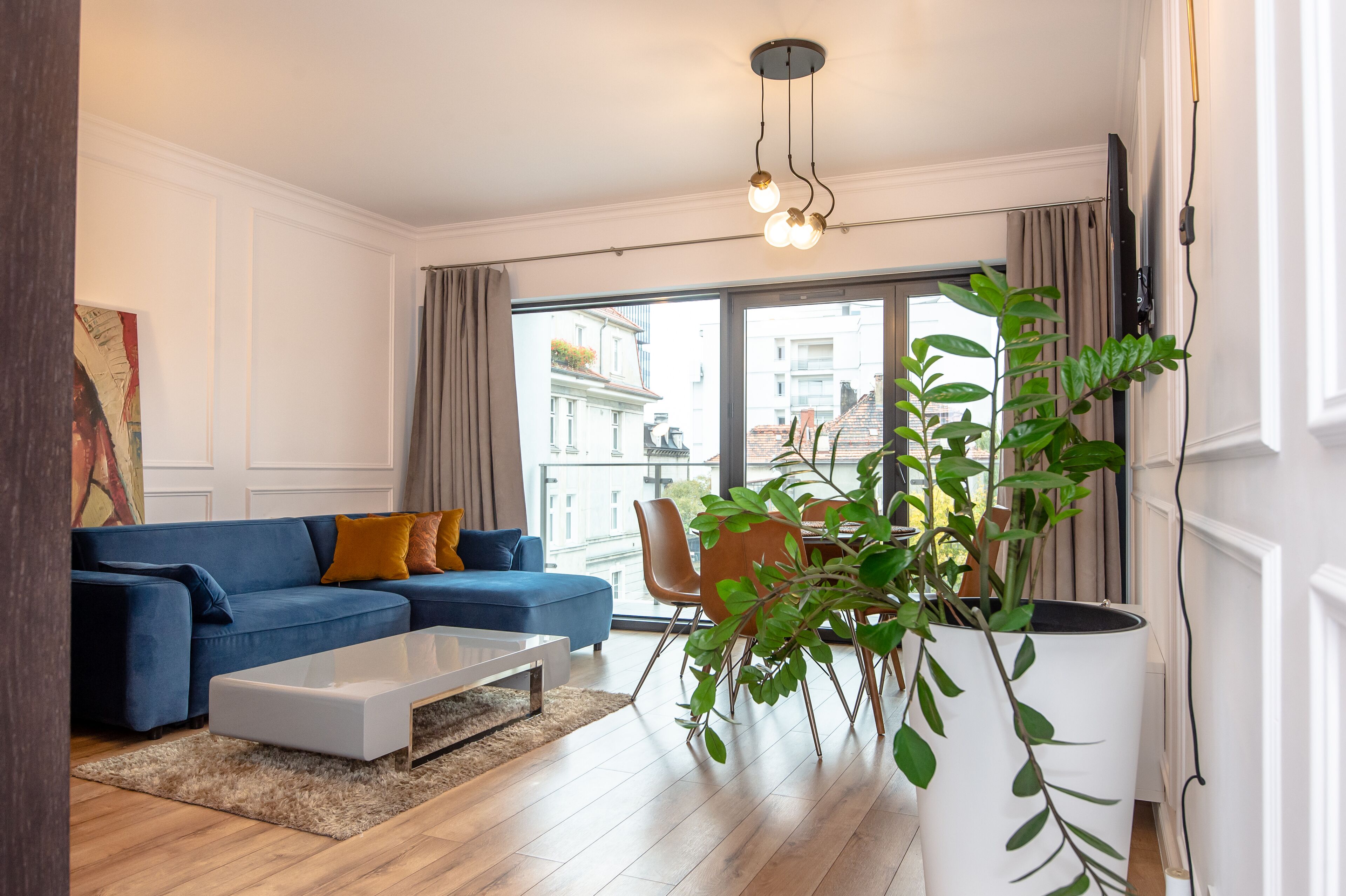 A modern living room with a blue sofa, white coffee table, and a large window with curtains.