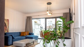 A modern living room with a blue sofa, white coffee table, and a large window with curtains.