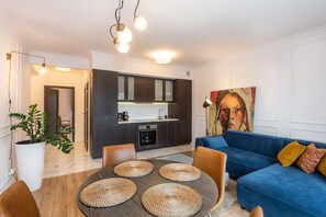 Una sala moderna con un sofá azul, una mesa de comedor con individuales tejidos y una cocina con armarios oscuros y una encimera blanca.