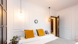 A neatly arranged bedroom with a large bed, two bedside tables, a wall clock, and a door leading to another room.