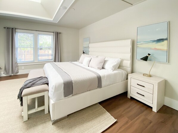 Une chambre moderne avec un grand lit, une table de chevet, un banc et une fenêtre avec des rideaux.