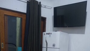 Ein Zimmer mit einem weißen Kühlschrank, einer Holztür, einem an der Wand befestigten Fernseher und einem Bambusboden.
