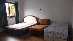 Ein Zimmer mit zwei Betten, einem Vorhangfenster, einem Wandventilator und Holzboden.