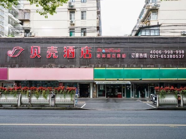 A hotel with a prominent red and white sign, a green awning, and a row of potted plants in front.