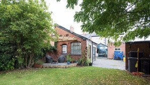 A residential property with a brick house, a paved driveway, and a garden area with a lawn and some trees.