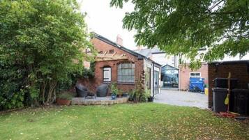 A residential property with a brick house, a paved driveway, and a garden area with a lawn and some trees.