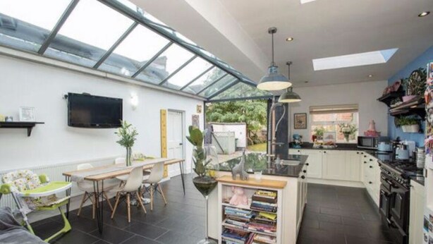 A modern kitchen with a large island, a dining area with a high table, and a TV mounted on the wall.
