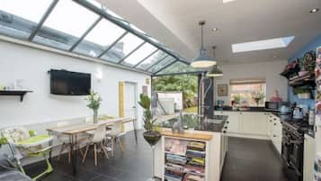 A modern kitchen with a large island, a dining area with a high table, and a TV mounted on the wall.
