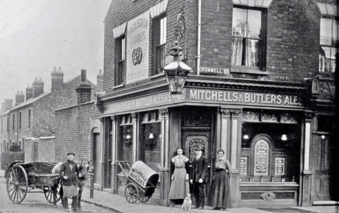 Una escena de calle antigua con un edificio que dice "MITCHELLS & BUTLER'S ALES".