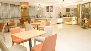 A modern hotel dining area with tables and chairs, a kitchen in the background, and a large window with curtains. - City Comfort Inn Yuzhou Dayuxiang (Xuchang)