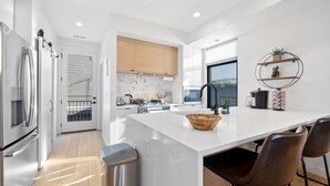 A modern kitchen with white cabinetry, a large island, stainless steel appliances, and a view to the outside.