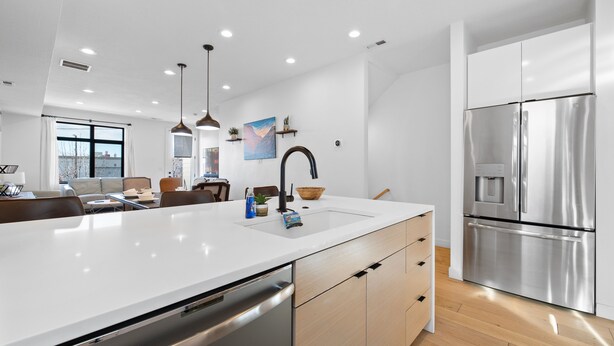 A modern kitchen with a stainless steel refrigerator, a large island with a sink, and wooden cabinets.