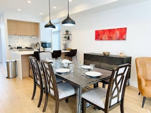 A modern dining area with a wooden table and chairs, a dark-colored cabinet, and a red abstract painting on the wall.
