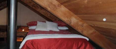 A bedroom with a sloped ceiling, a bed with red bedding, and a wooden beam structure.