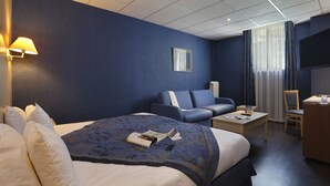 A hotel room with a large bed, a sofa, a desk, and a television.