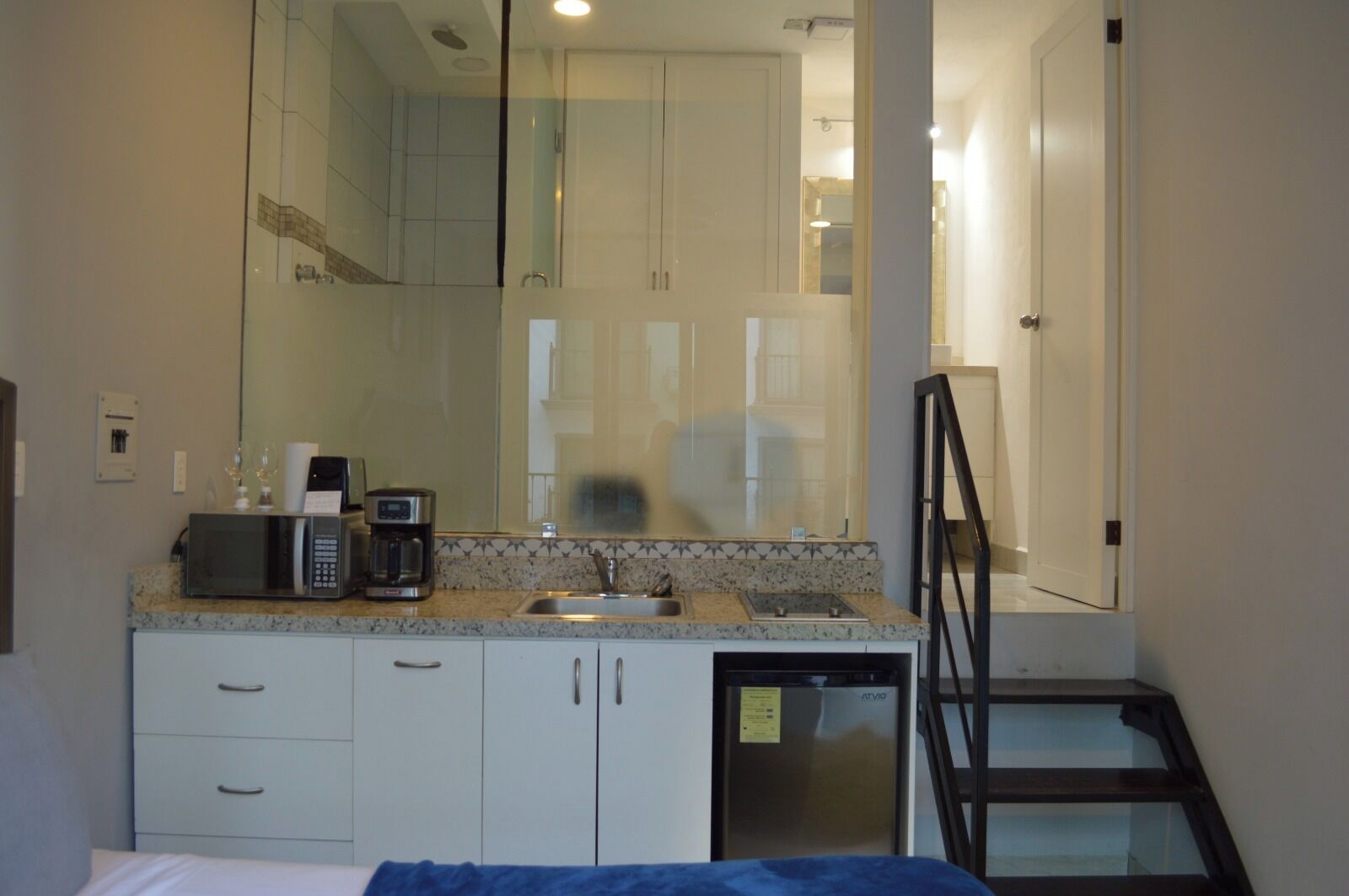 A compact hotel room with a kitchenette, a bed, a small refrigerator, and a window with a view of the street.