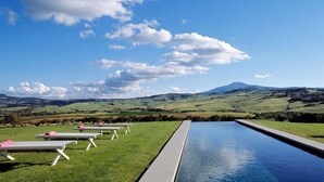 A poolside area with lounge chairs and a view of rolling hills and a mountain in the distance.