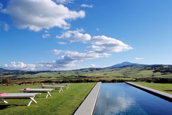 Zona junto a la piscina con sillones de descanso y vistas a colinas ondulantes y una montaña a lo lejos.
