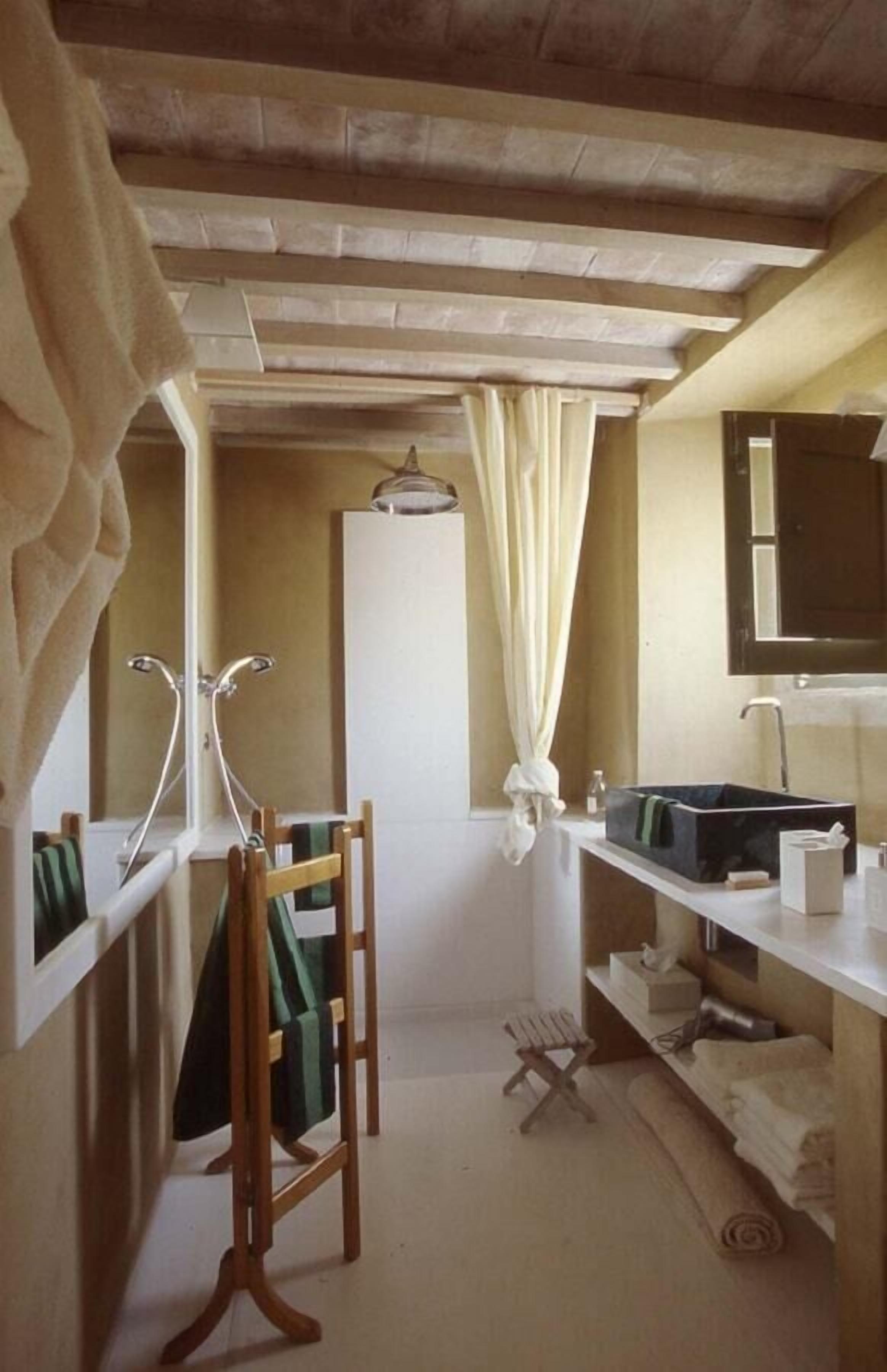 Een badkamer met een houten stoel, een handdoekhouder, een spiegel en een wastafel.