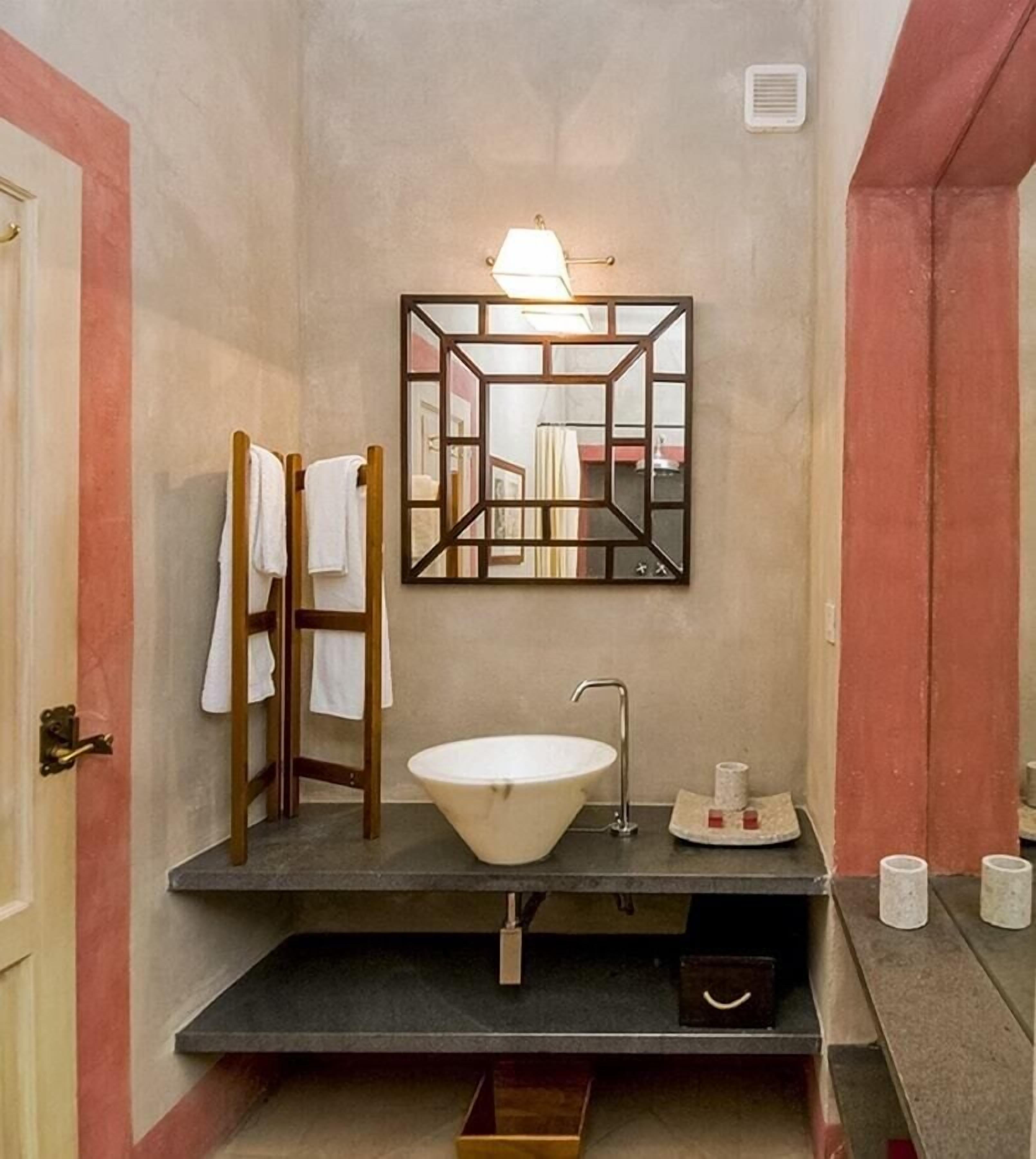 A bathroom with a freestanding bathtub, a wooden ladder, a towel rack, and a mirror with a geometric frame.