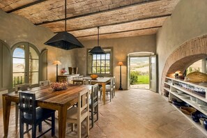 Un comedor rústico con una mesa y sillas de madera, una lámpara colgante negra y vistas al exterior a través de un ventanal grande.