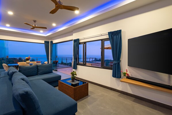 A modern living room with a large flat-screen TV, a sofa, a coffee table, and a balcony with a view of the sea. - Tropical Villa a new stunning sea view Villa (Koh Samui)
