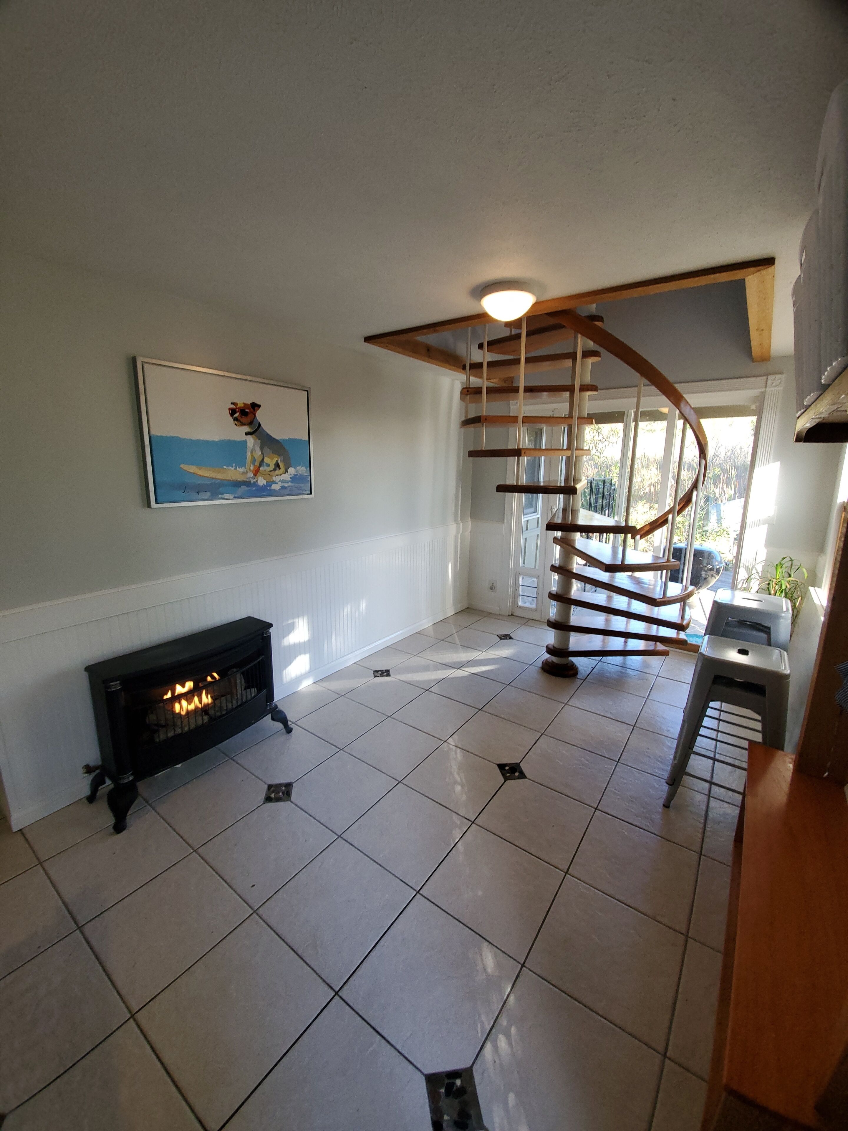 A spacious room with a fireplace, a spiral staircase, and a painting of a dog surfing.