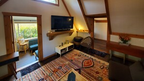 A cozy attic room with a sloped ceiling, a television mounted on a wooden beam, a patterned rug, and a small seating area with a chair and a table. - Tip of the Peninsula Lake House Retreat (South Bend)