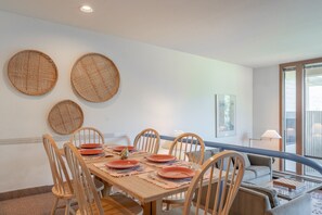 Un comedor con una mesa de madera dispuesta para seis personas, rodeada de sillas de madera. Hay tres cestas tejidas en la pared sobre la mesa.