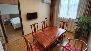 Une chambre d’hôtel avec une table à manger en bois, quatre chaises, un téléviseur fixé au mur, un lit et une plante en pot.