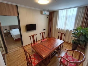 Une chambre d’hôtel avec une table à manger en bois, quatre chaises, un téléviseur fixé au mur, un lit et une plante en pot.