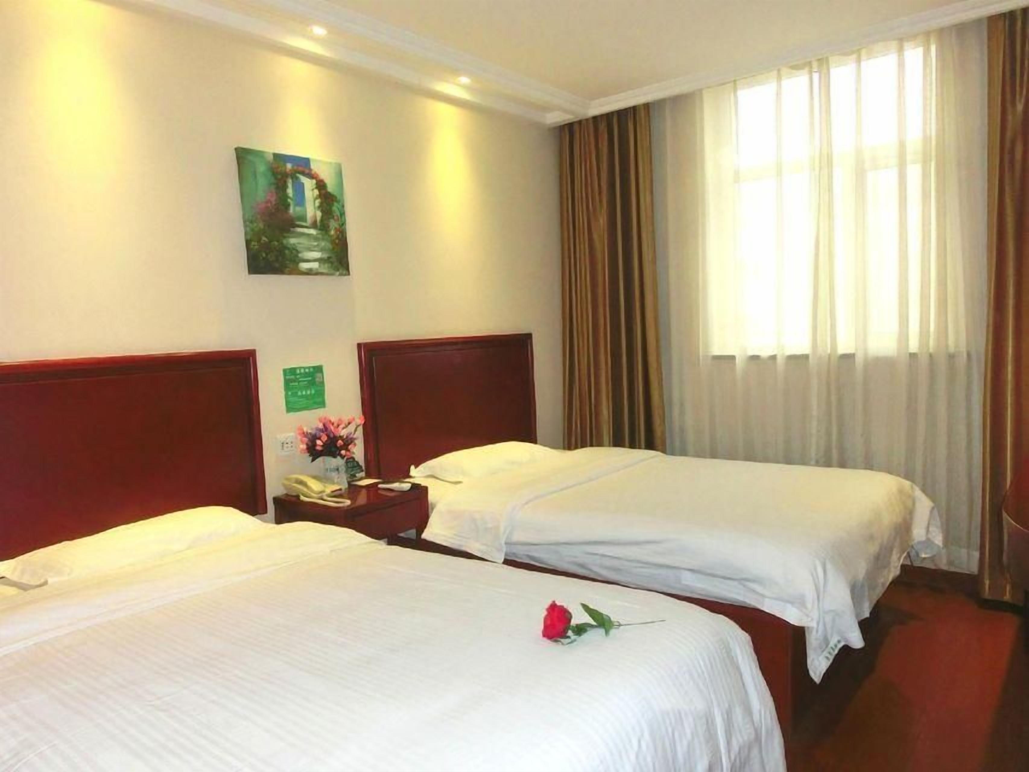 A hotel room with two single beds, a nightstand with a telephone and a vase of flowers, a painting on the wall, and a window with curtains.