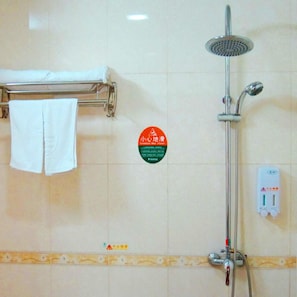 A bathroom with a shower, a towel rack with a white towel, and a caution sign on the wall.