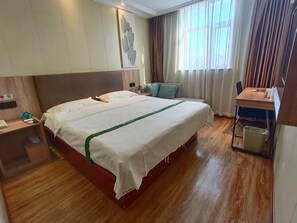 Une chambre d’hôtel avec un grand lit, un bureau avec une chaise, une petite table et une poubelle.