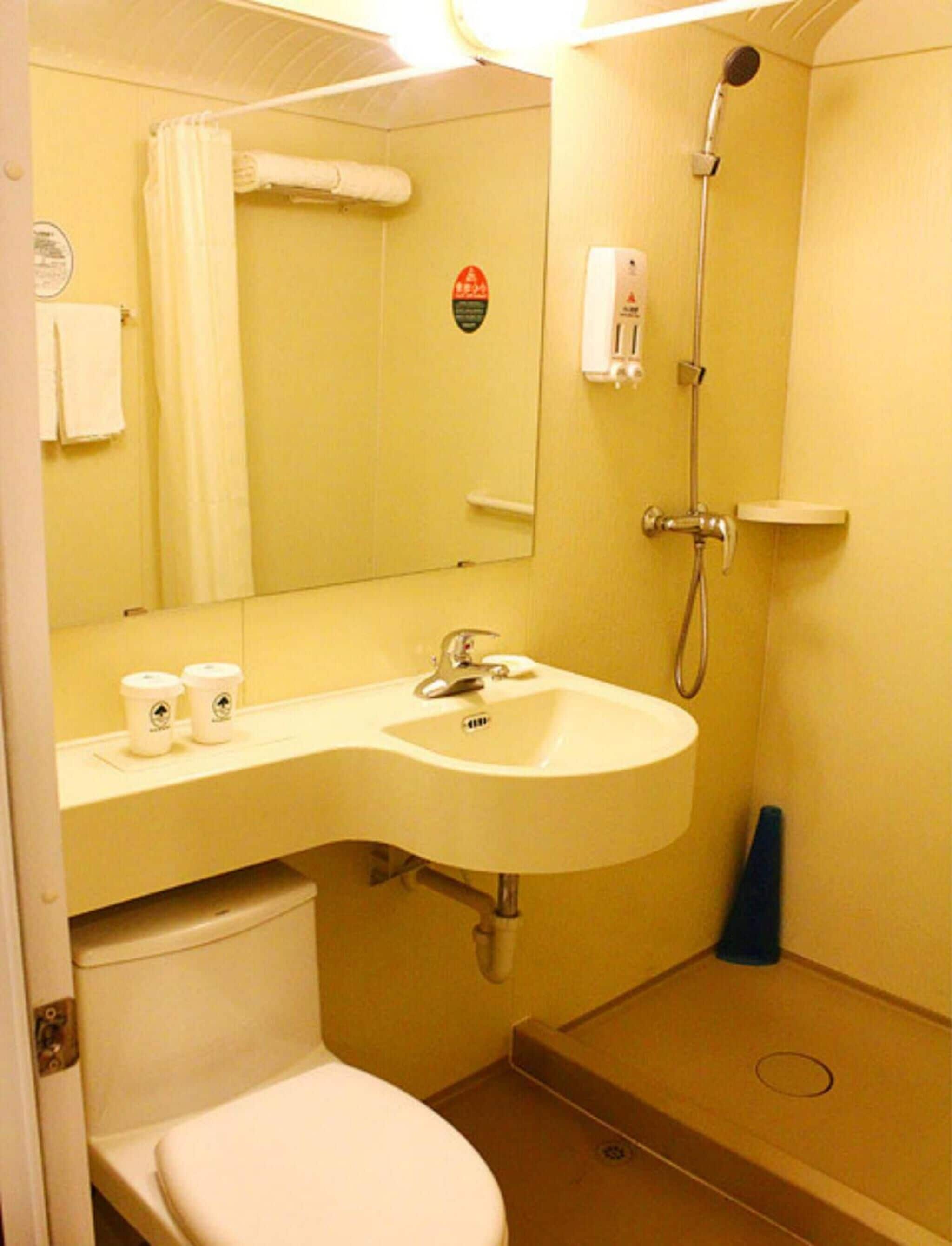 Ein kleines Badezimmer mit Toilette, Waschbecken und Dusche. Auf der Ablage des Waschbeckens stehen zwei Tassen.