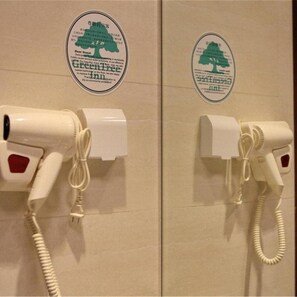 A restroom with two hair dryers mounted on the wall, each with a green tree logo sticker above them.