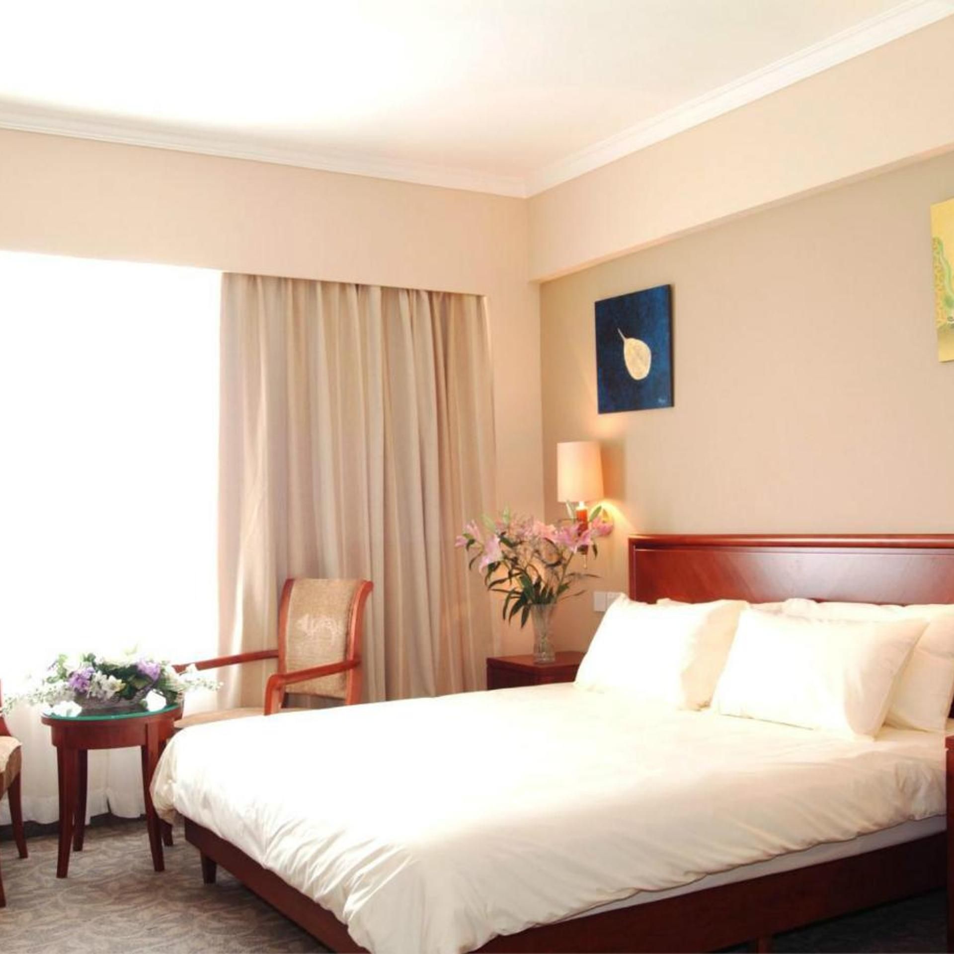 A hotel room with a bed, a chair, a nightstand, a lamp, and a window with curtains.