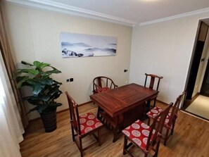 A dining area with a wooden table and four chairs, a large potted plant, and a wall-mounted painting.