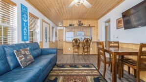 A cozy living room with a blue sofa, a dining table with chairs, and a kitchen area with wooden cabinets and a microwave. - Cabin 3, Aspen Leaf Lodges, Near Grand Lake (Grand Lake)