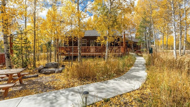 A wooden cabin with a deck, surrounded by trees with yellow leaves, a concrete path, and picnic tables. - Cabin 3, Aspen Leaf Lodges, Near Grand Lake (Grand Lake)